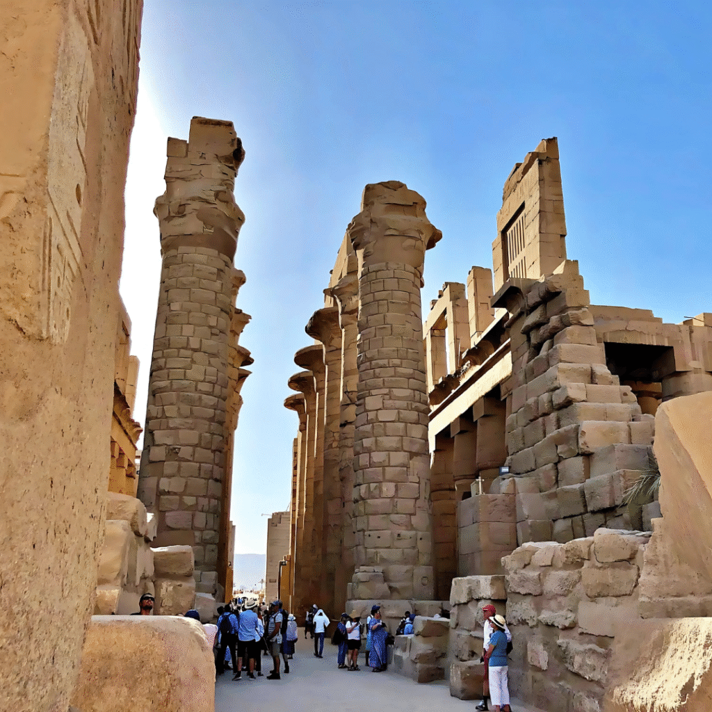 A breathtaking sunrise over the ancient Karnak Temple in Luxor, Egypt, with golden light illuminating massive stone columns and hieroglyphs, tourists exploring the site, the Nile River in the distance, realistic photography style, high detail, travel magazine quality.